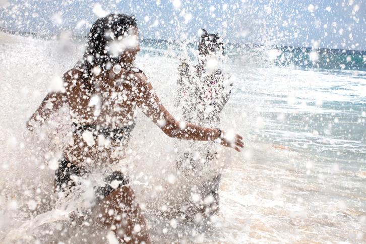 two women splashing white ocean foam as they run into the ocean